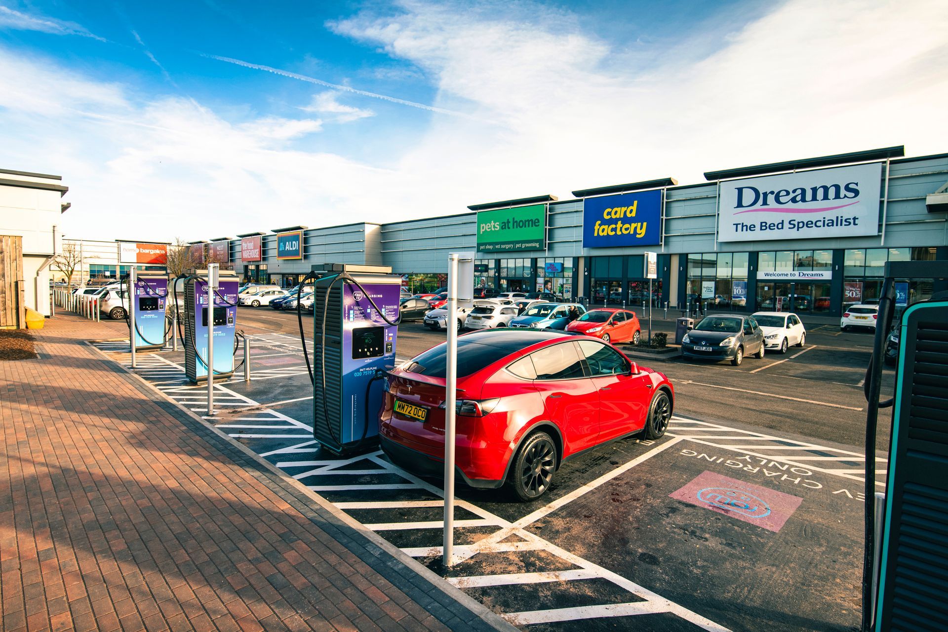 A red car is parked in a parking lot in front of a store.