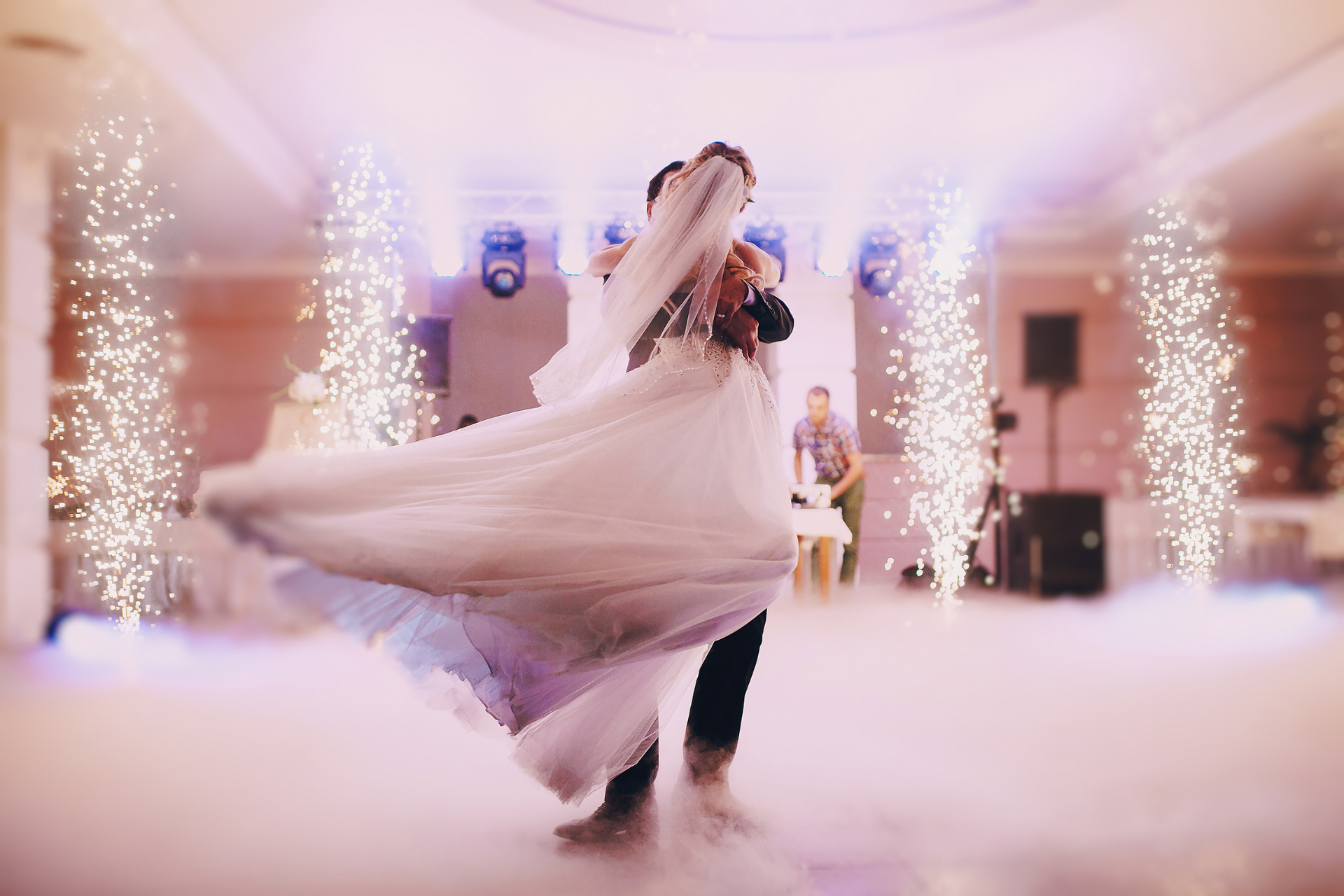 A couple dancing in a ballroom filled with floor-level fog, surrounded by glowing vertical pyrotechnic sparks.