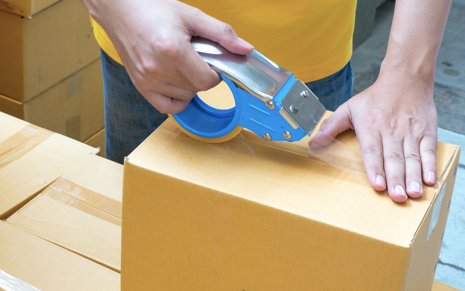 A person is taping a cardboard box with a blue tape dispenser.