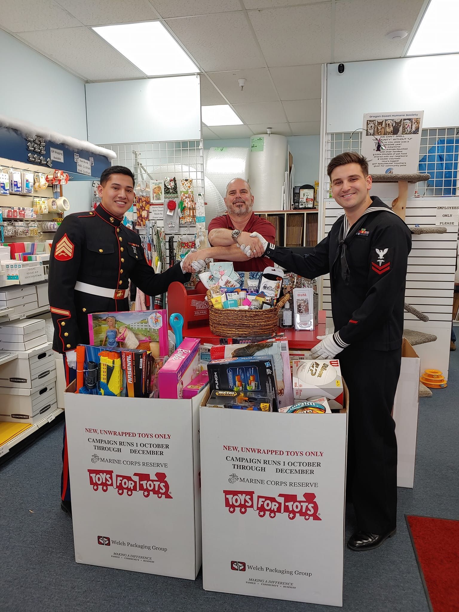Three men in military uniforms are standing in a store with boxes full of toys.