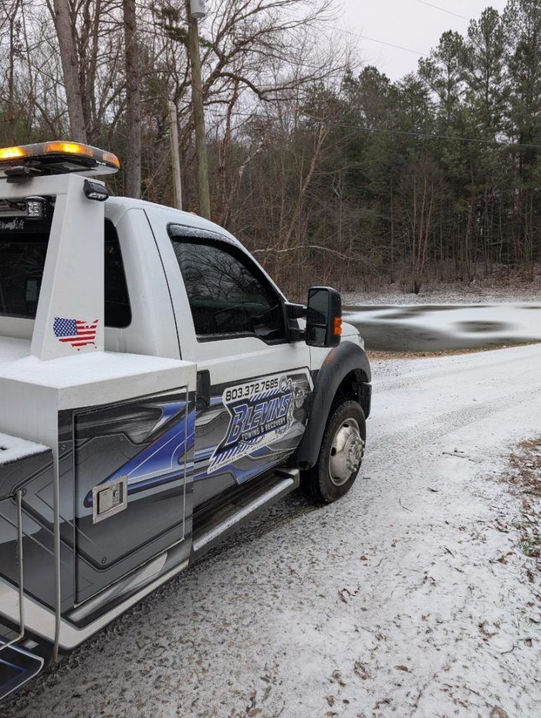 White tow truck on a snowy roadside near a curve in the woods