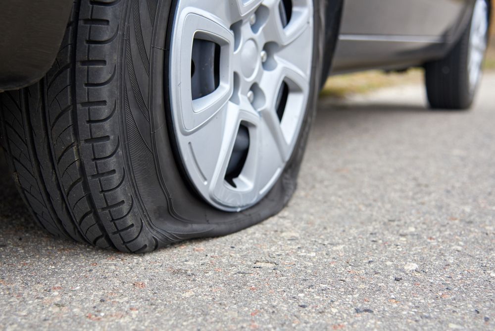 Flat tire on a silver car parked on asphalt, with the wheel rim close to the ground.