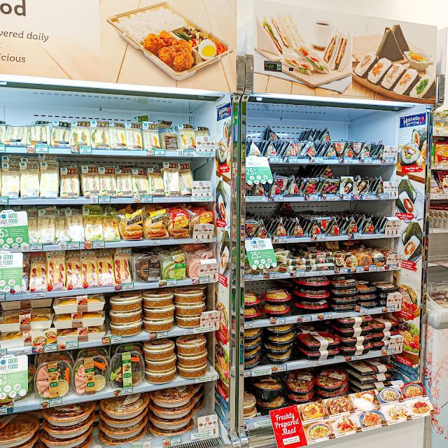 Refrigerated shelves stocked with pre-packaged food at a convenience store. Includes sandwiches, rice balls, and other ready-to-eat meals.