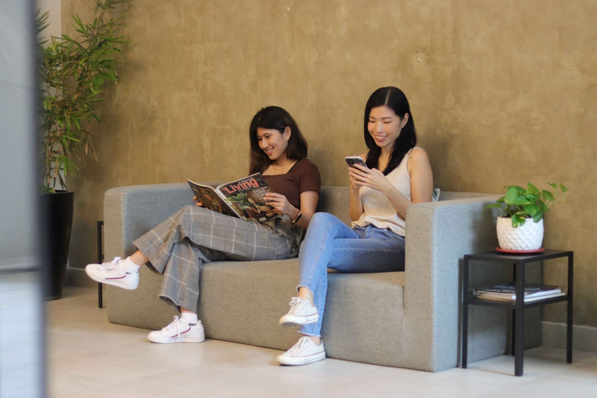 Two people sitting on gray sofas, looking at their phones in a modern lounge