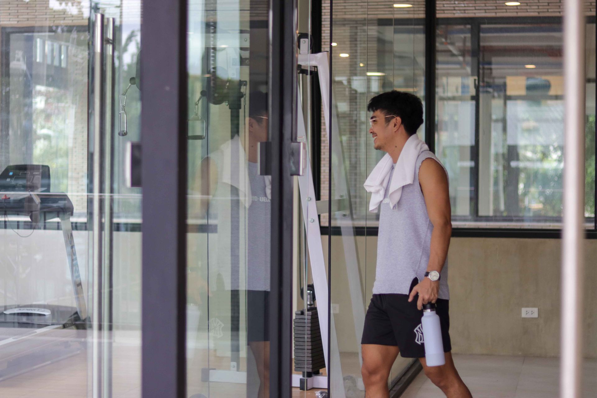 Man in gym clothes exits a gym, holding a water bottle and towel.