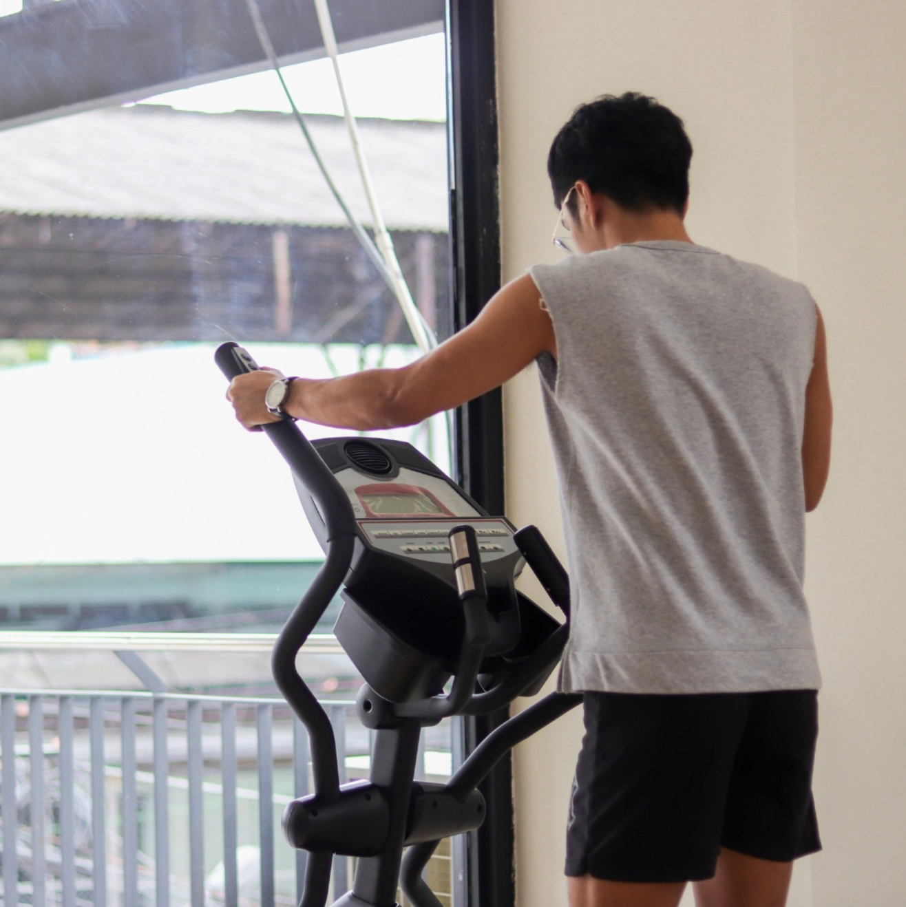 A man is using an elliptical machine in front of a window at the gym