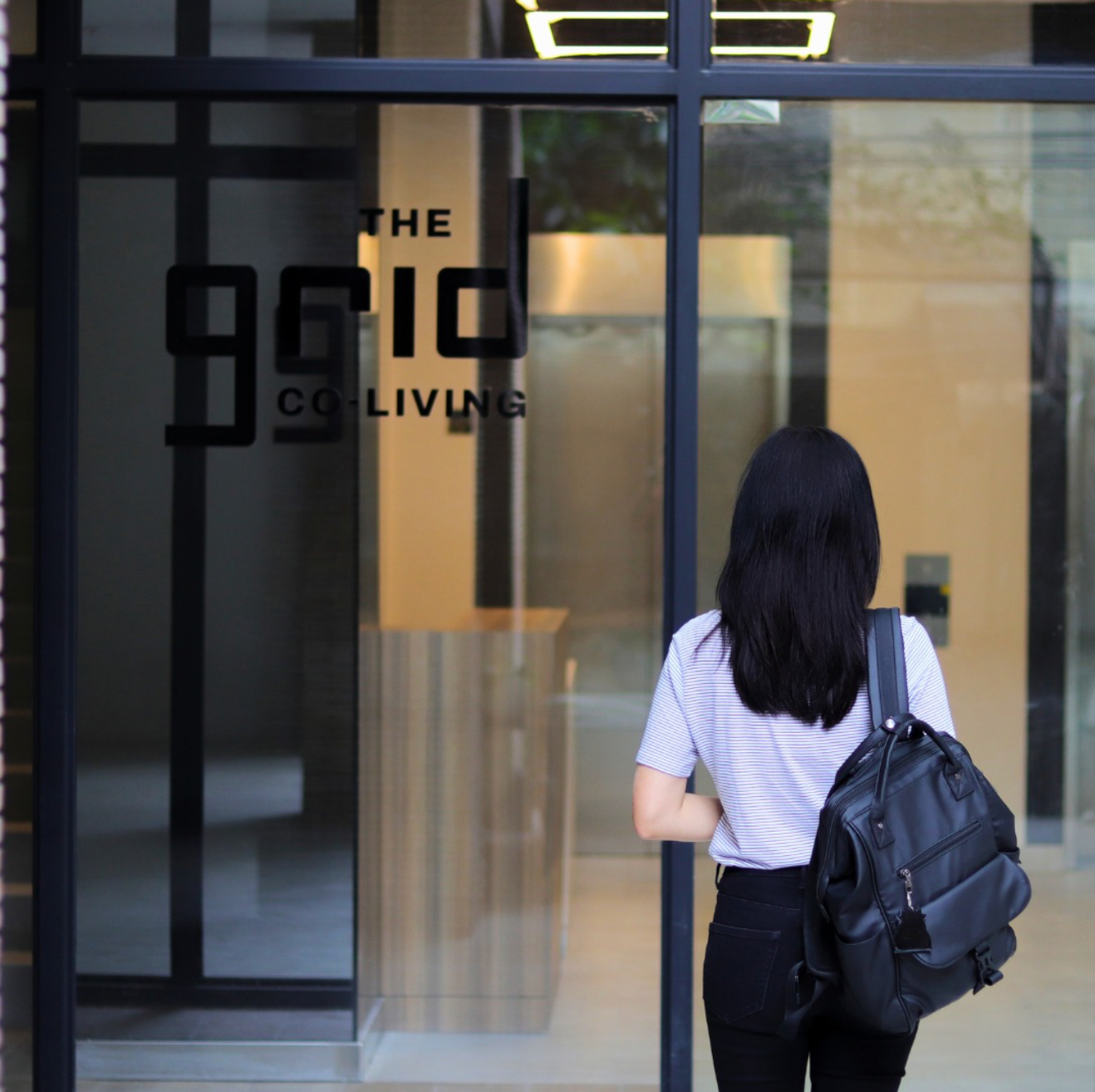 A woman standing in front of a glass door of the grid co living