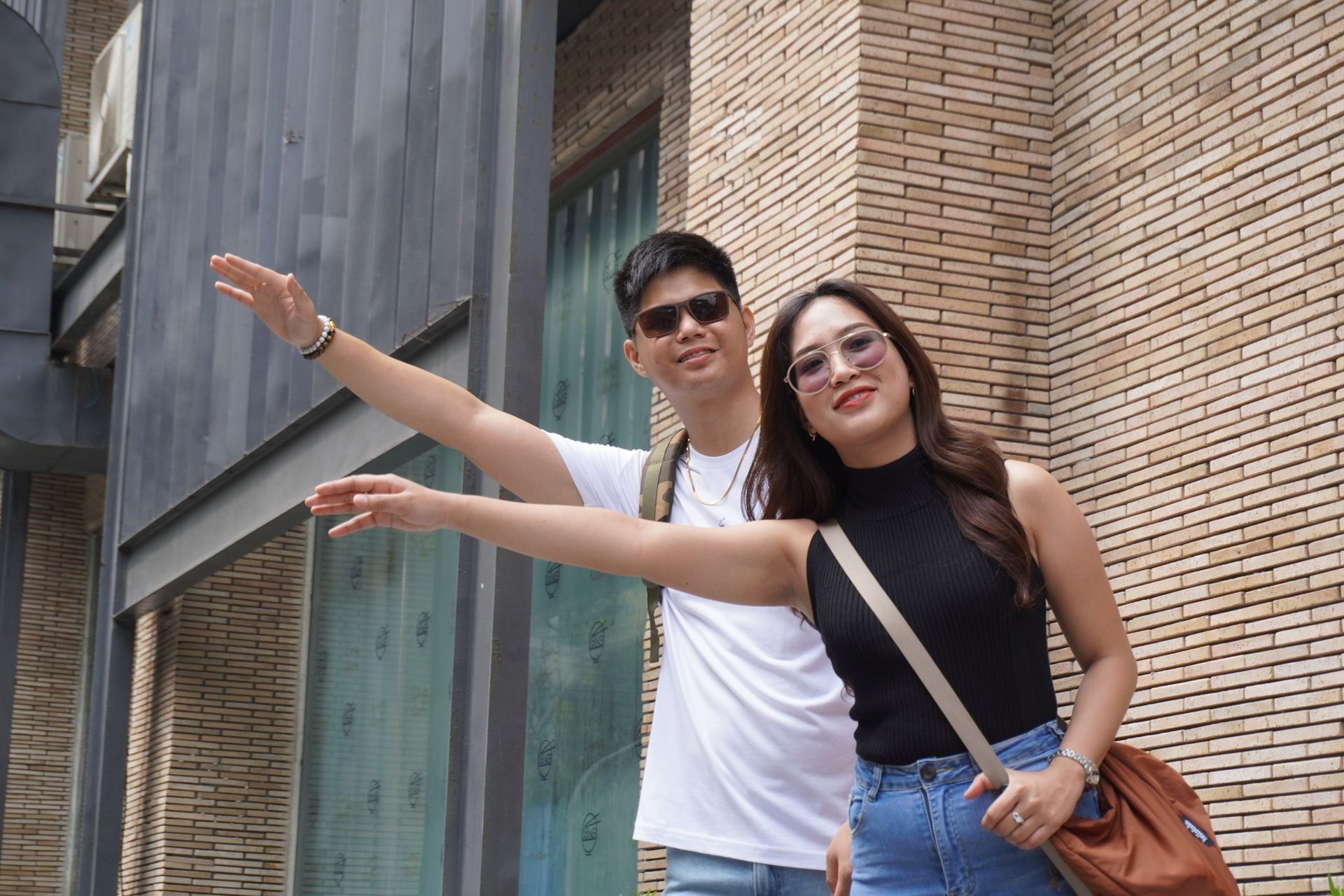 Two people hailing a cab outside The Grid Makati dormitory; smiling, wearing sunglasses, with one arm raised.