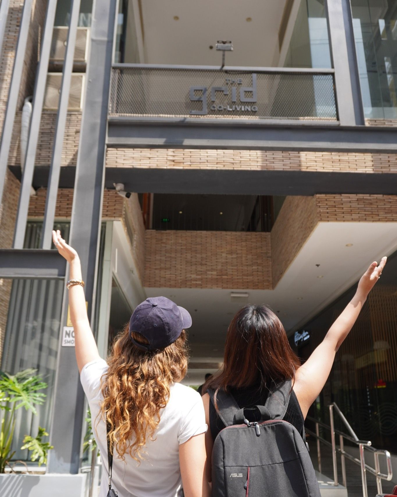 Two women with arms raised, in front of a dorm in Makati