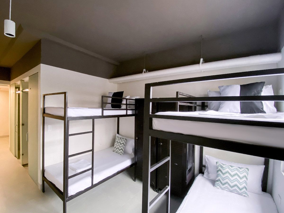 Bunk beds in a hostel room with white bedding and gray accents; a closet and hallway are visible.