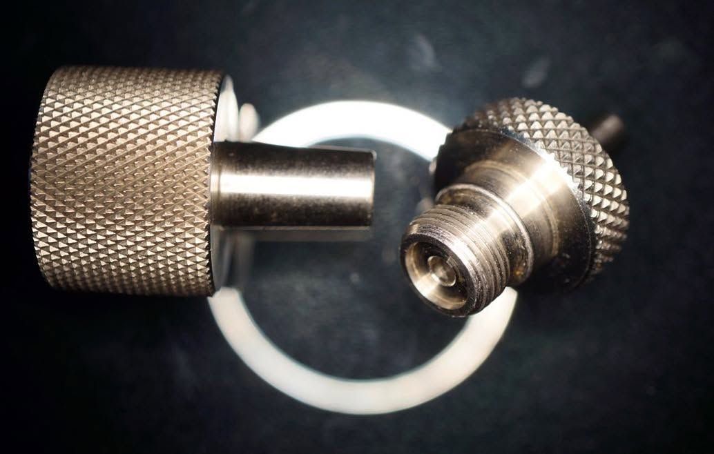 Close-up of a metallic knurled connector and matching cap on a black background.