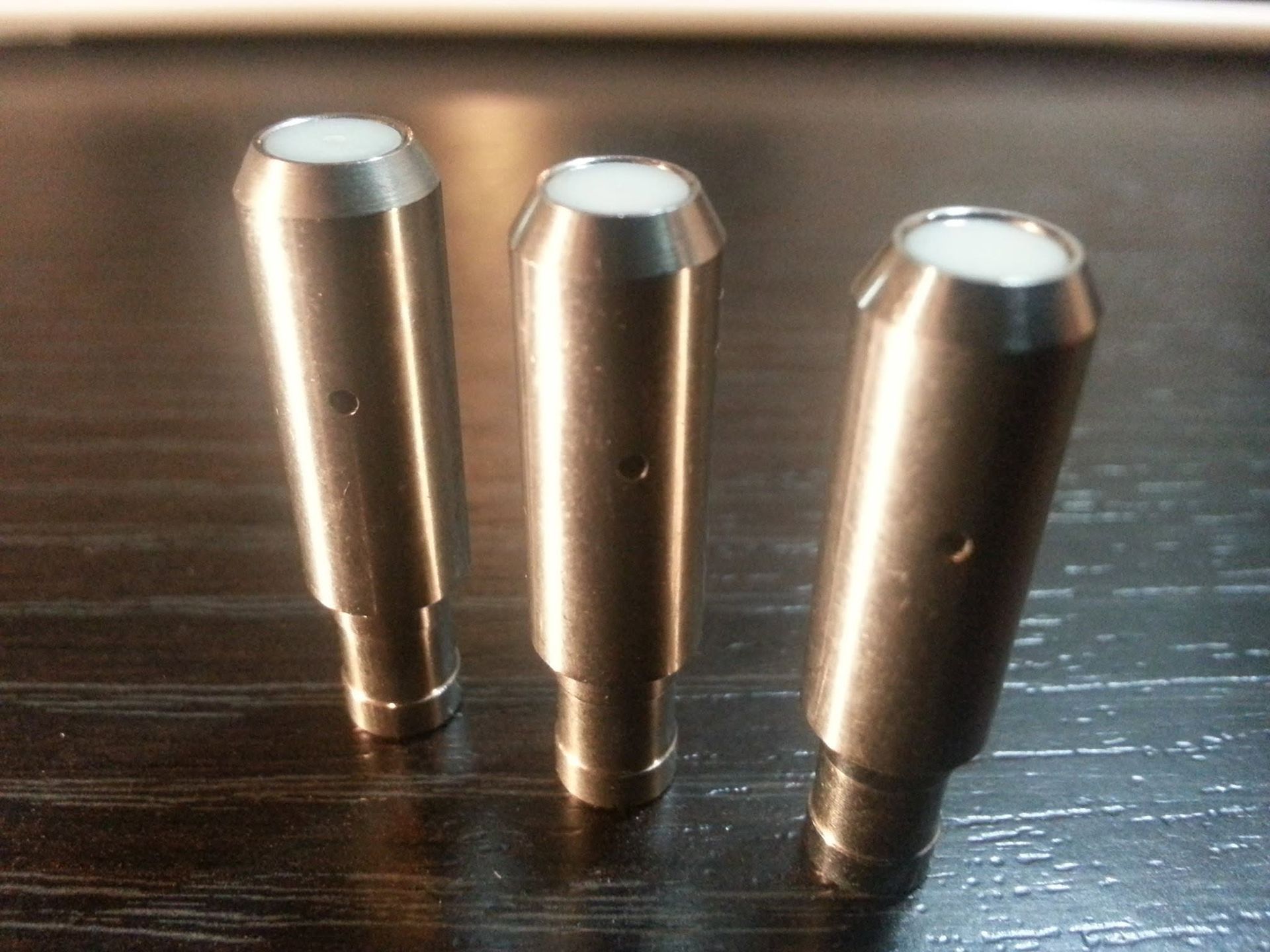 Three metallic cylindrical pegs standing upright on a dark wooden surface