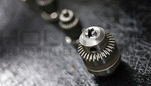 Close-up of metallic drill bits and a gear-like tool on a dark textured surface