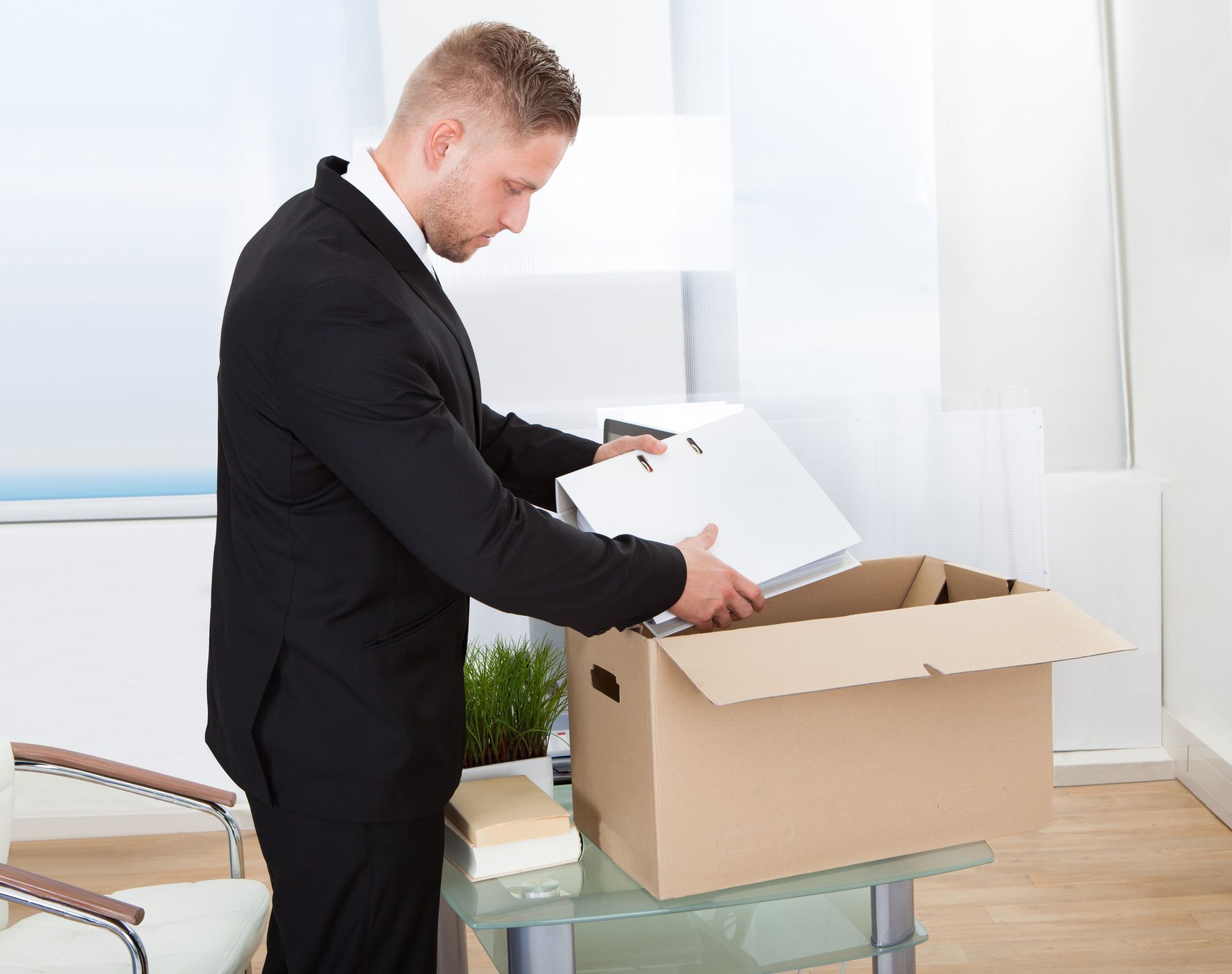 a man in a suit is packing his belongings into a cardboard box .