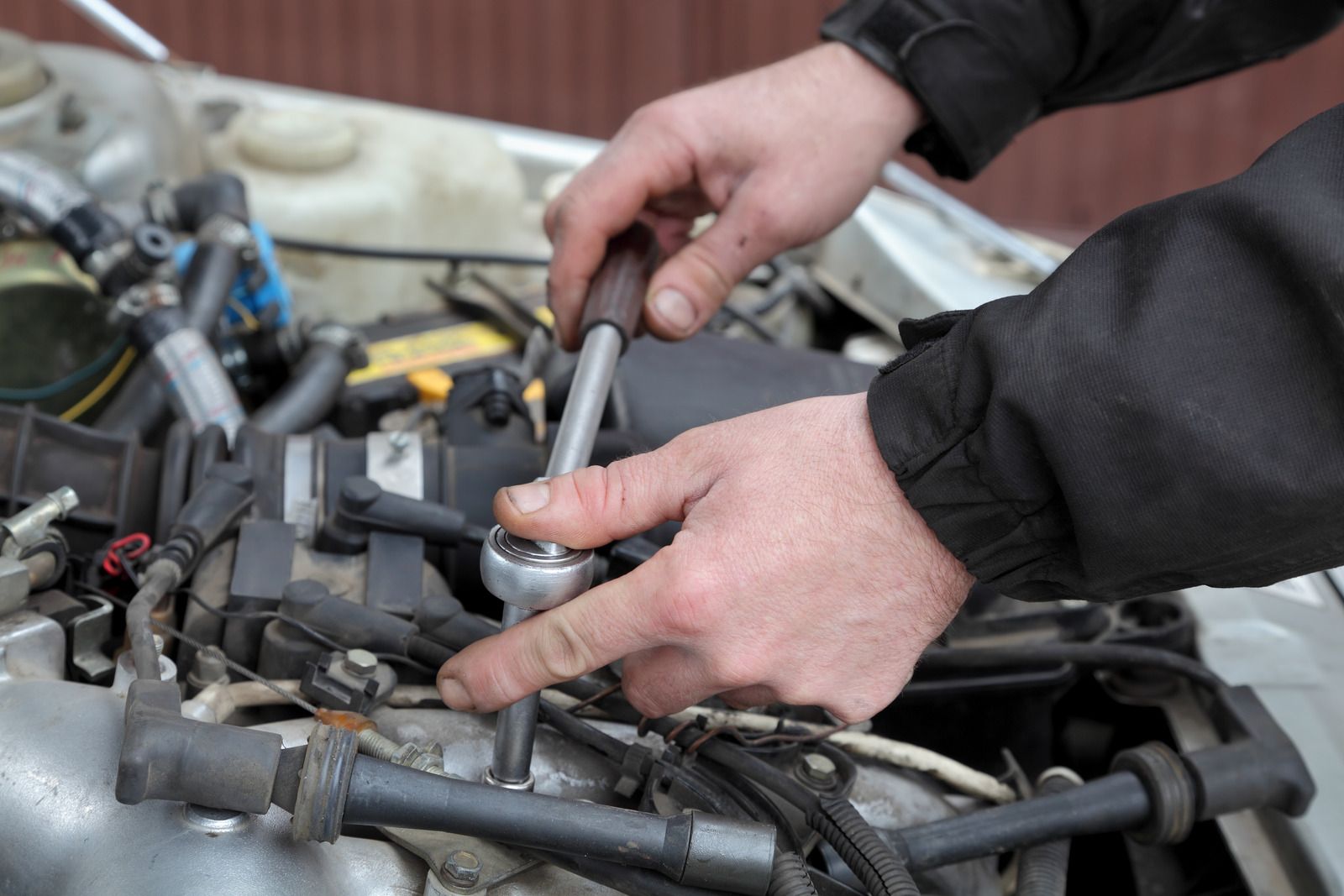 A man is working on a car engine with a wrench.