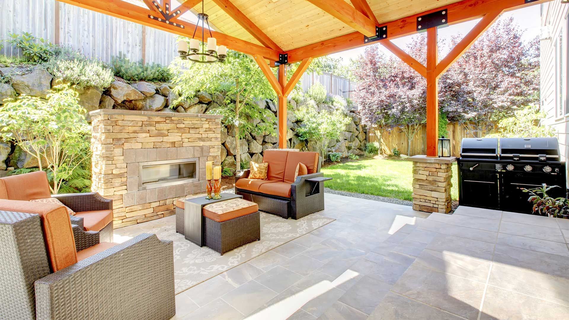 A patio with furniture and a fireplace under a wooden roof.