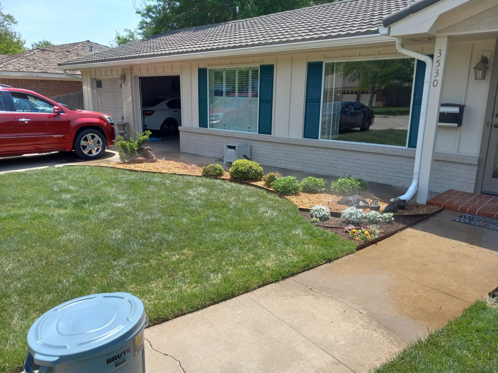 Suburban house with a red car in the driveway and landscaping in front.