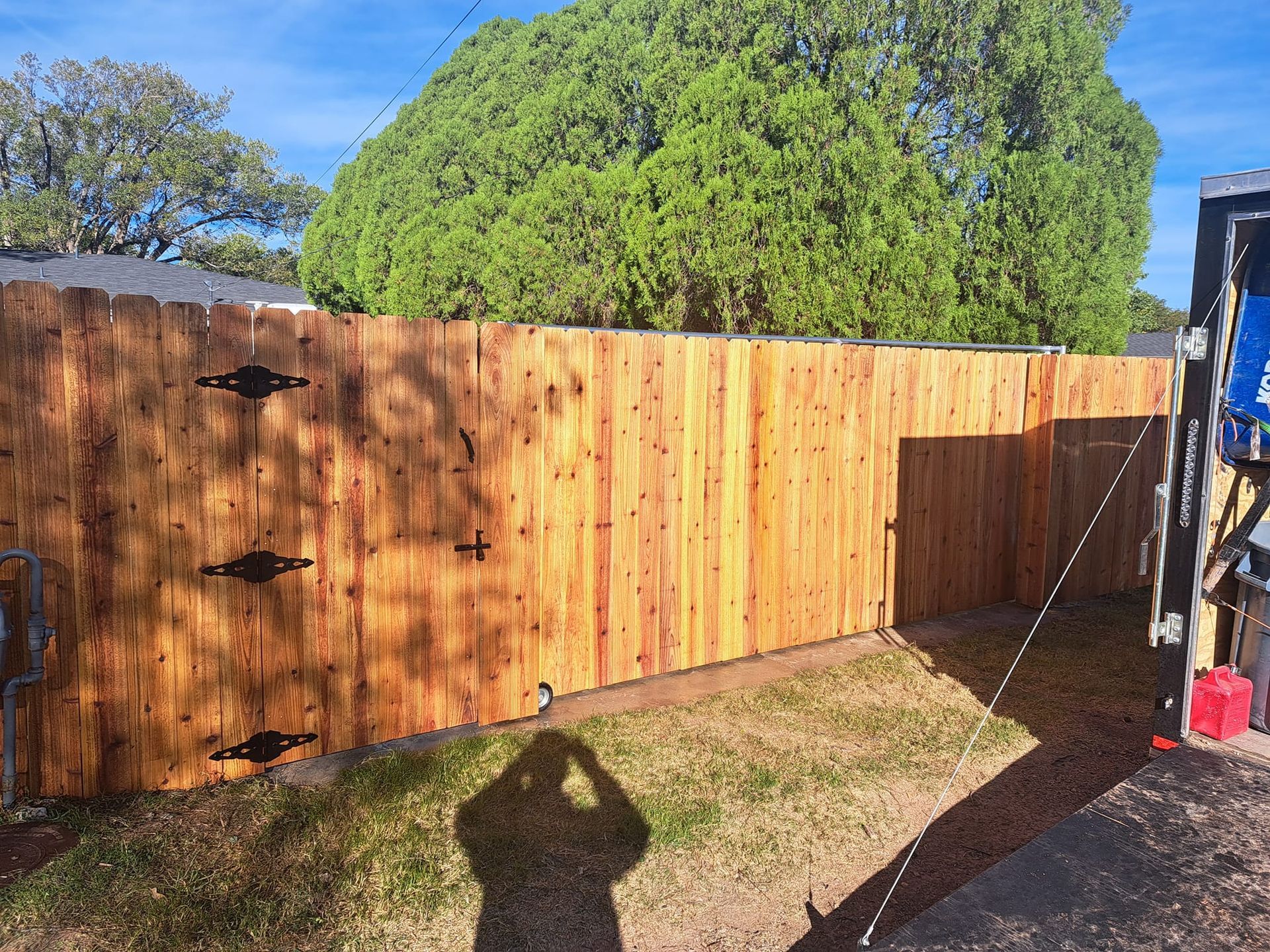 Wooden fence with decorative hardware; sunlight casts shadows on the ground and fence.