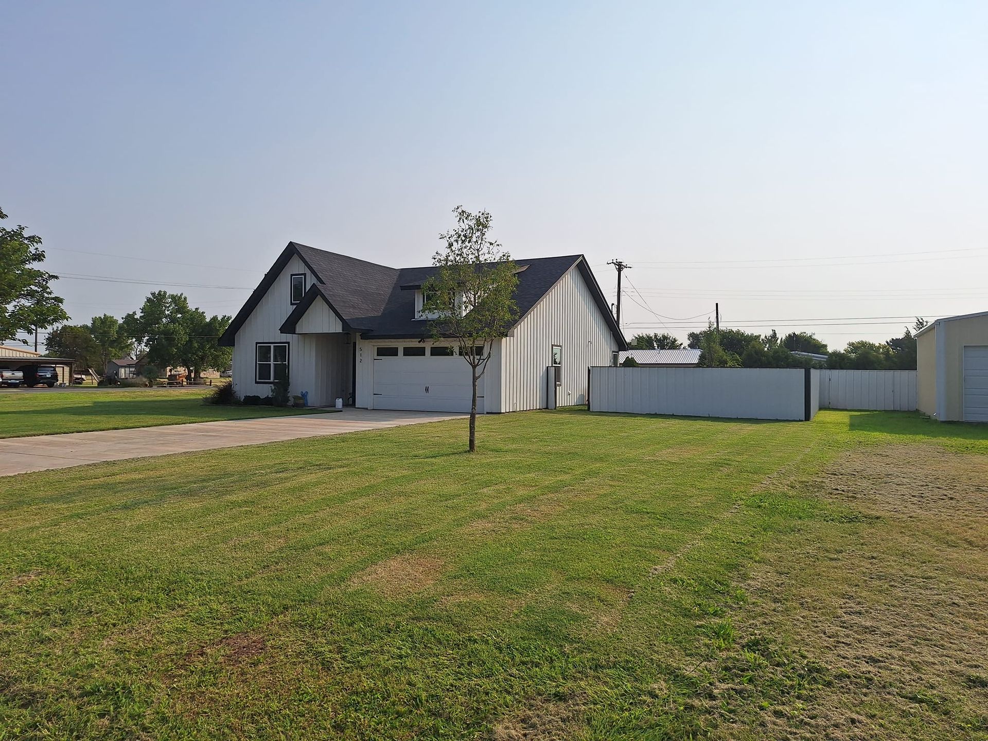 White house with dark roof and attached garage, in a grassy yard under a blue sky.
