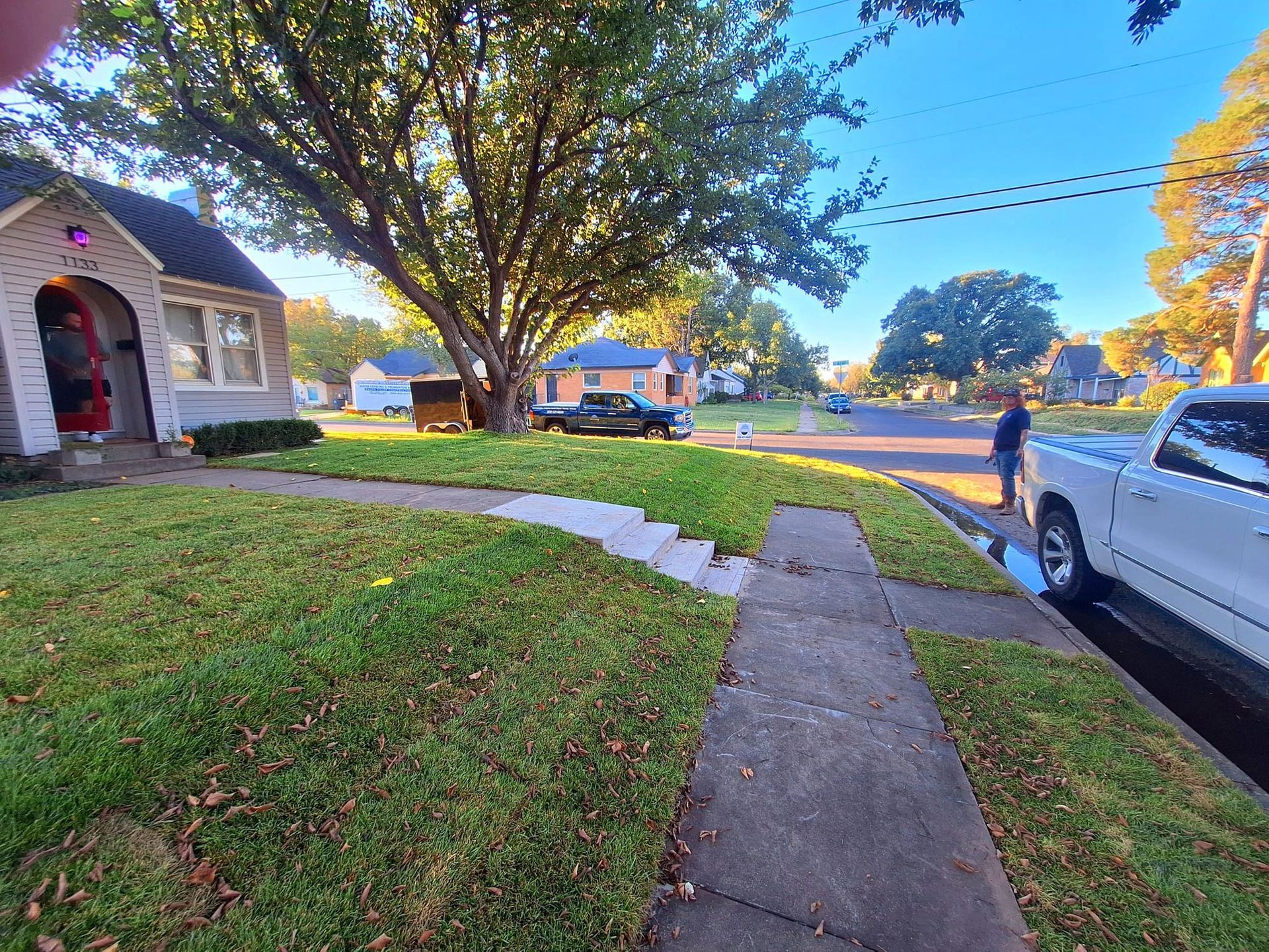 A white house and sidewalk with a lawn. A person stands near a white truck on a sunny day.