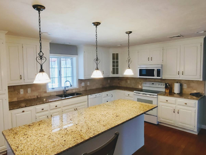 Bright white kitchen with granite island, pendant lights, and microwave over stove