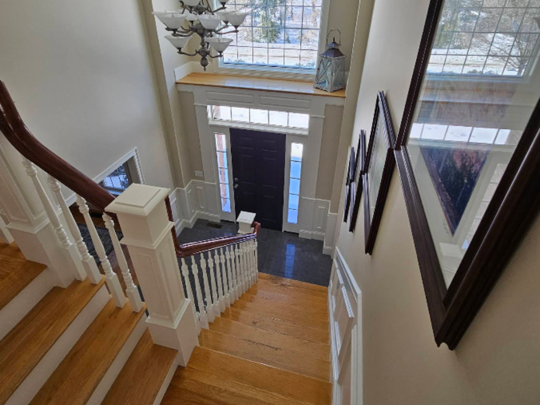 Staircase with white railings and wood steps leading to a front door in a bright foyer