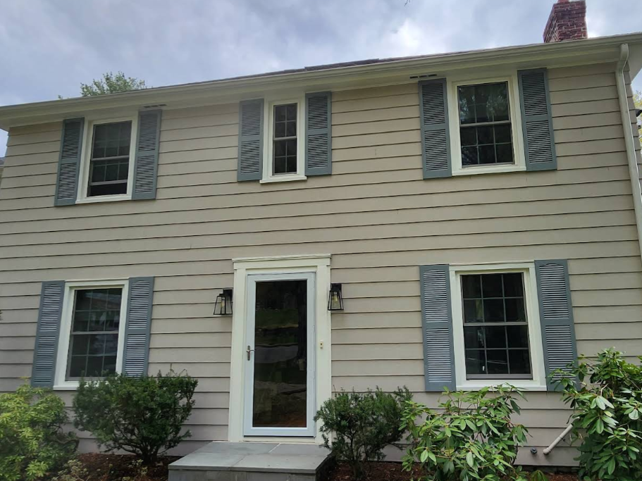 Two-story beige house with white trim, blue shutters, and a front door centered on the facade.