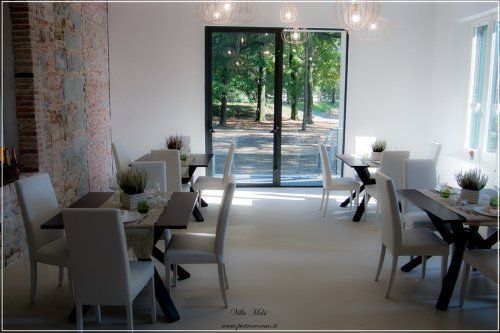 Sala luminosa con vetrate, tavoli e sedie bianche