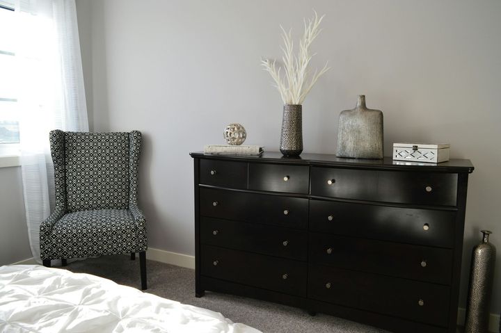 A bedroom with a black dresser and a chair