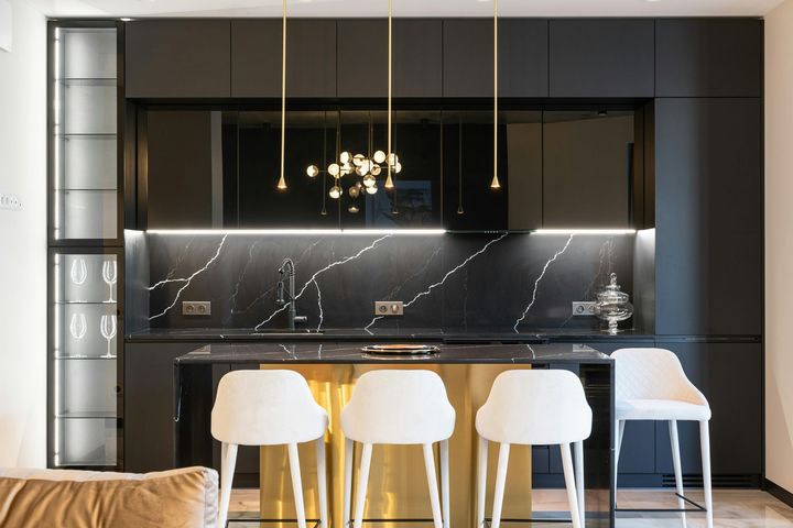 A kitchen with black cabinets , a gold island , and white stools.