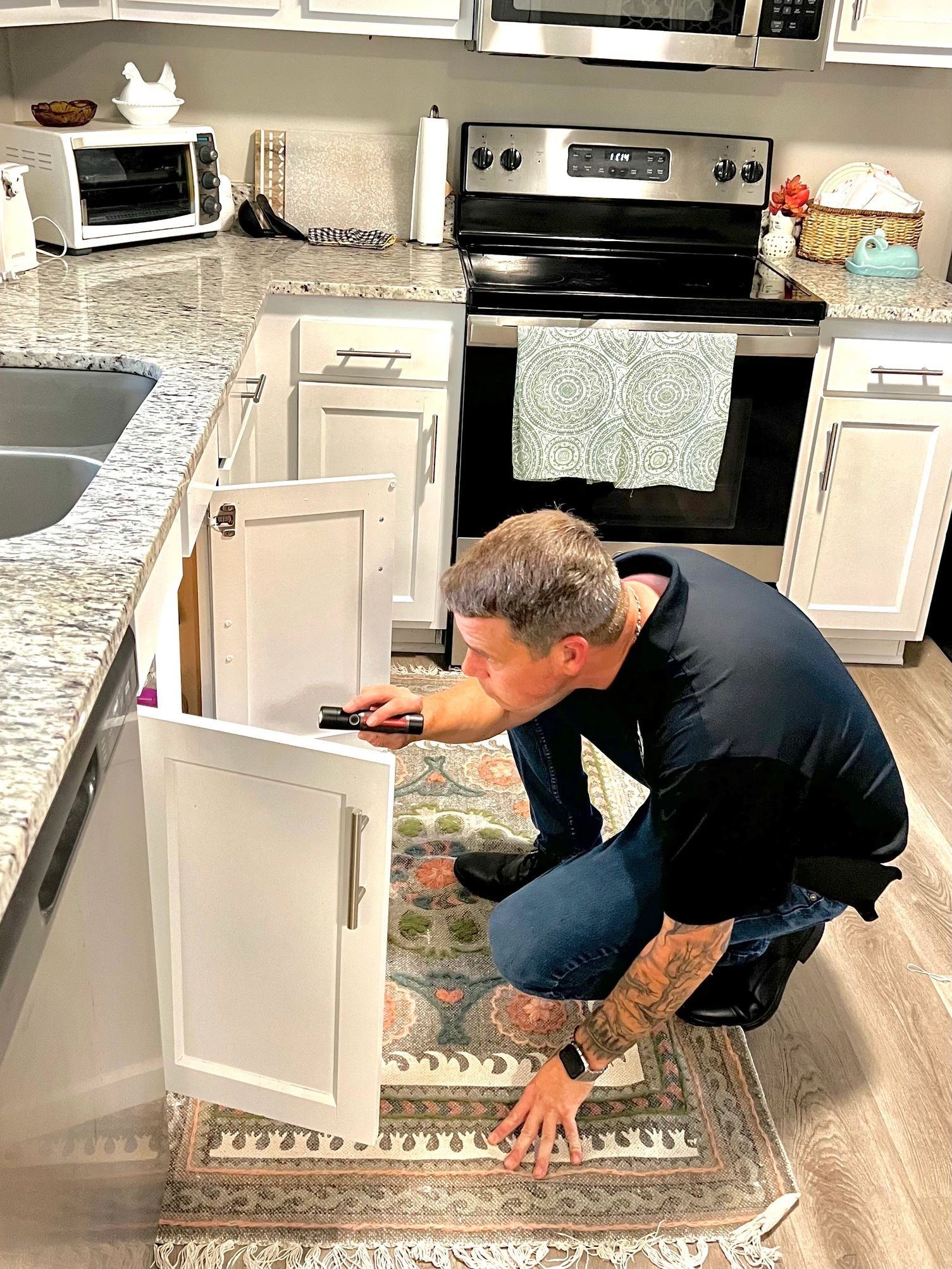 A man is kneeling down in a kitchen looking under a sink.