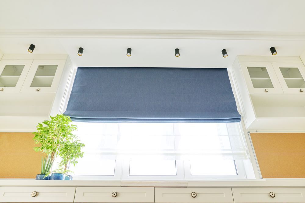 A Kitchen Window With a Blue Roman Shade and White Cabinets — Curtain Haven & Blinds in Port Macquarie, NSW