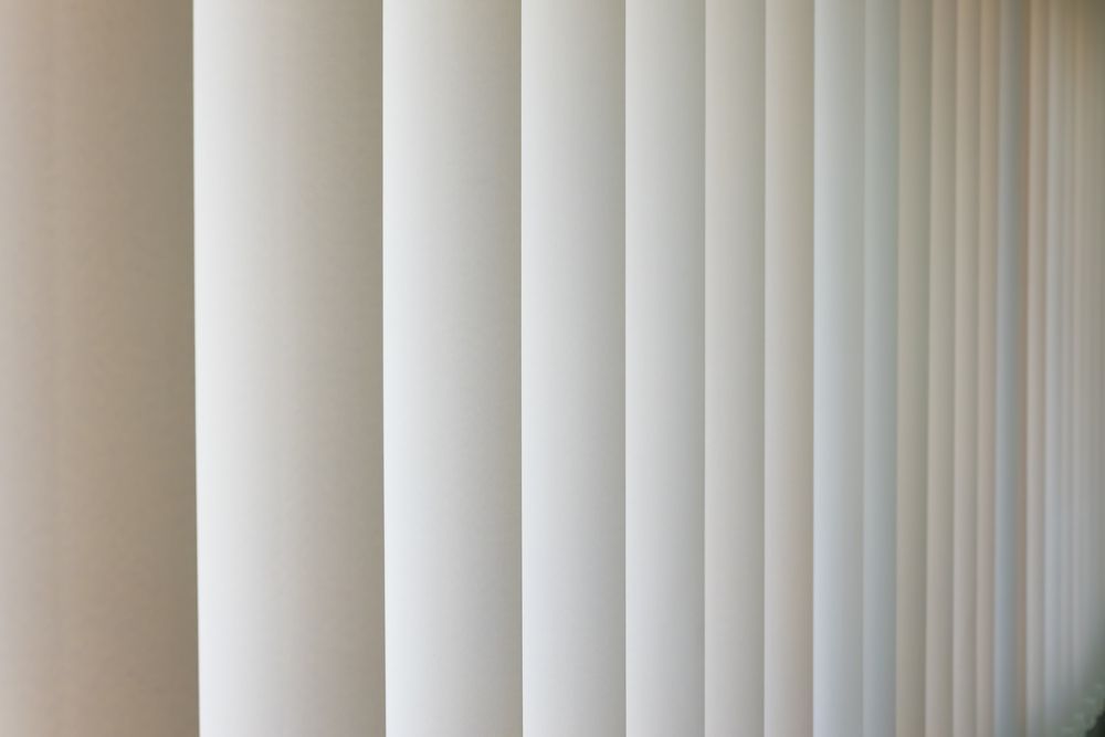 A Close Up of a Row of White Vertical Blinds on a Wall — Curtain Haven & Blinds in Laurieton, NSW
