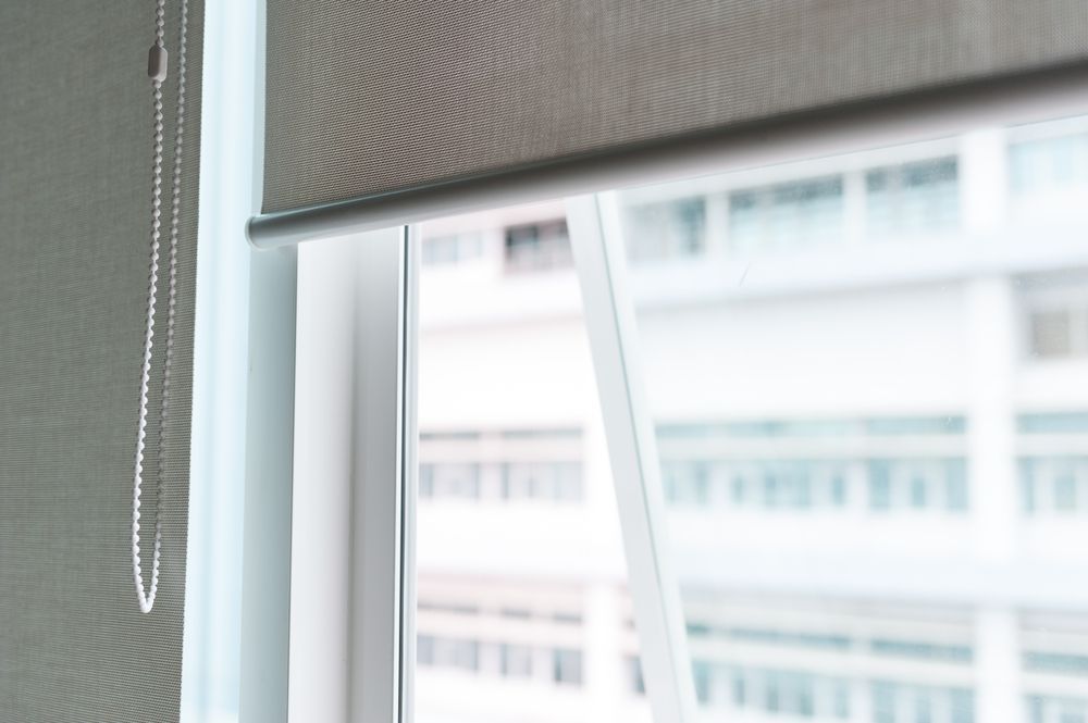 A Close Up of a Roller Blind on a Window With a Building in the Background — Curtain Haven & Blinds in Laurieton, NSW