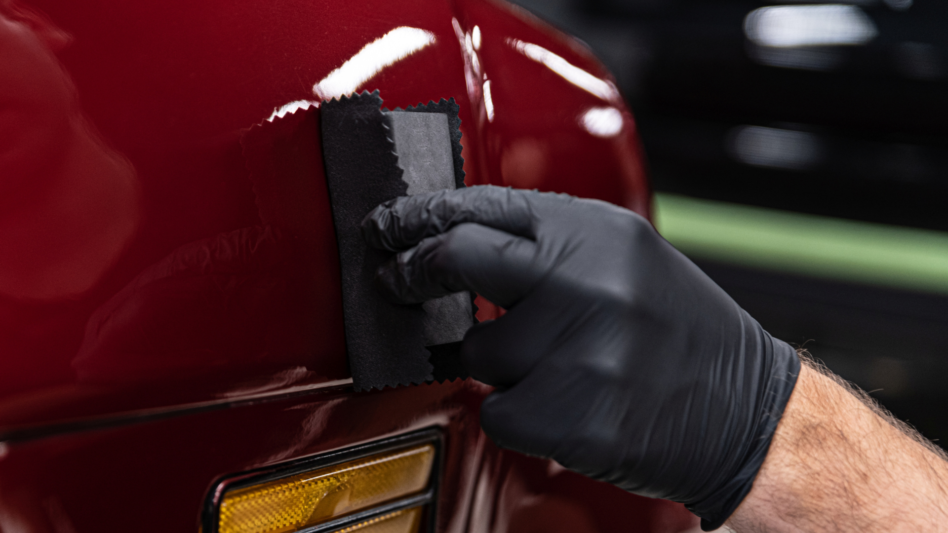 A person wearing black gloves is polishing a red car with a sponge.