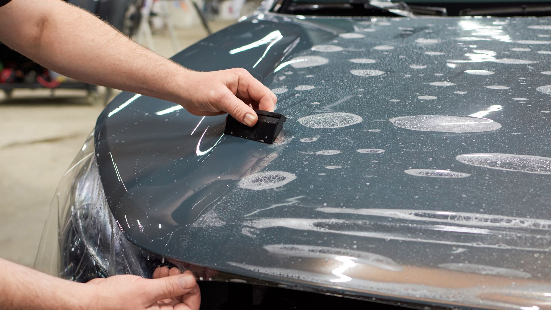 A person is applying protective film to the hood of a car.