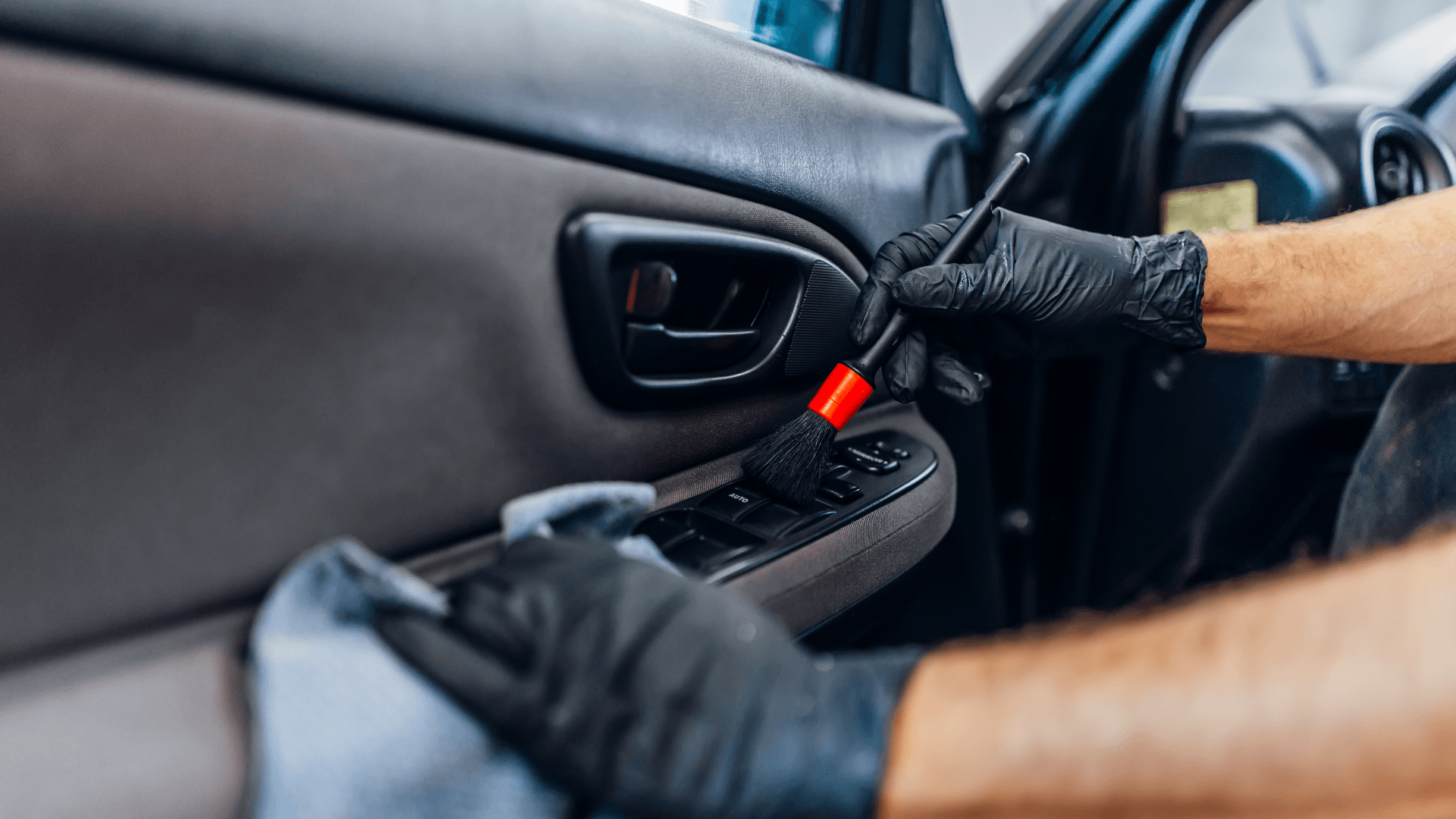 A man is cleaning the interior of a car with a brush.