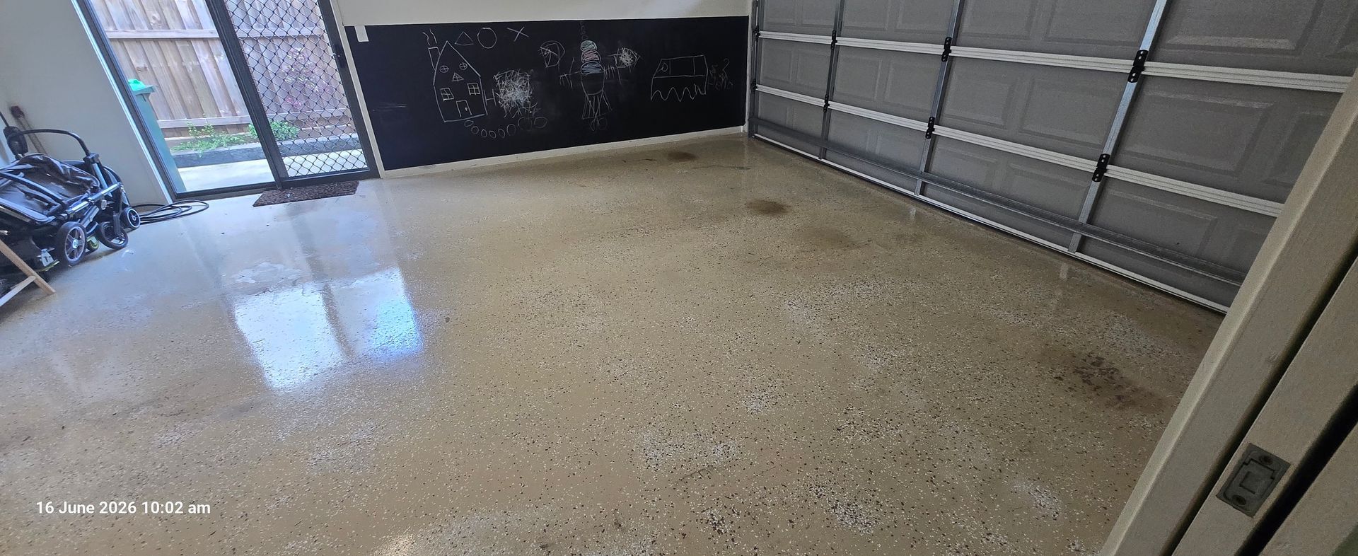 Garage interior with speckled epoxy floor, gray sectional door, and open walkway to the outside.