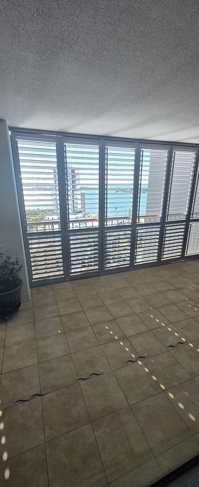 Balcony with gray tile floor and white louvered shutters overlooking a city view.