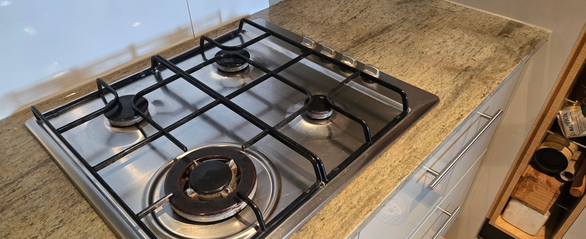 Gas cooktop on a beige kitchen countertop with a black grate and stainless steel burners.