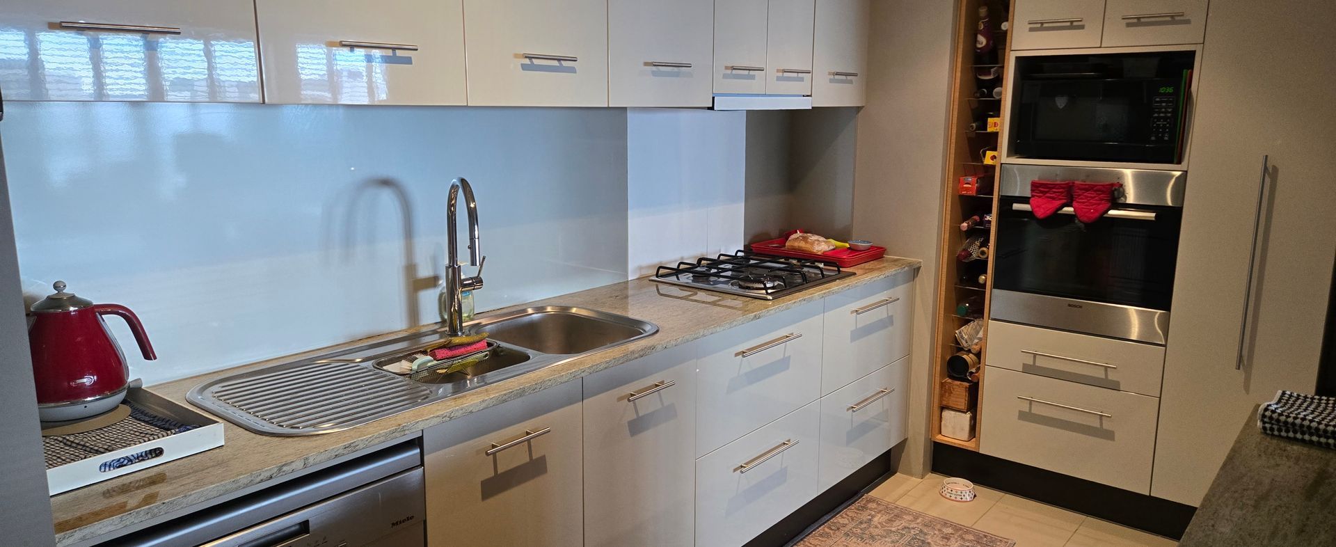 Modern kitchen with stainless steel appliances, white cabinets, sink, stove, and red kettle on the counter