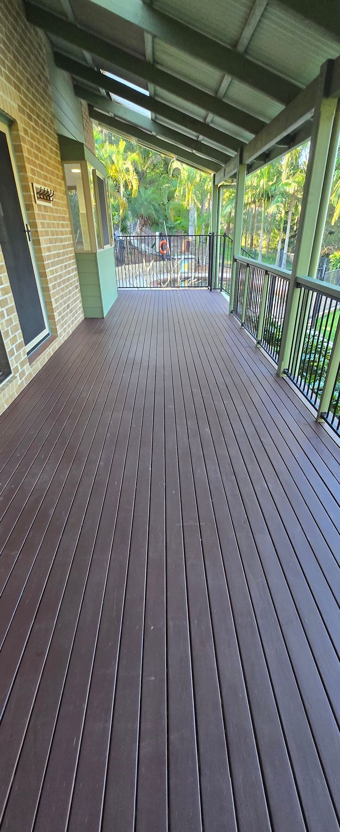 Covered wooden porch with brown decking, green railings, and a view of trees outside
