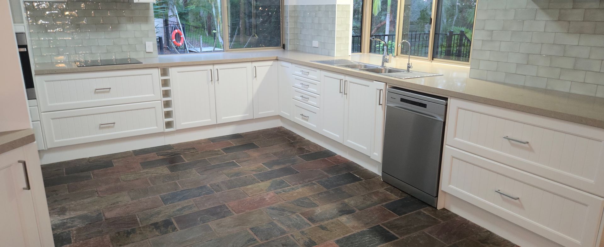 Bright kitchen with white cabinets, dark tile floor, and a large window over the counter