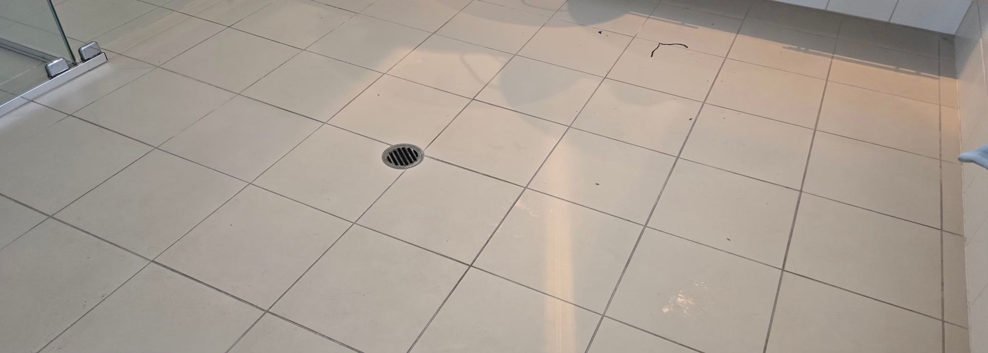 White tiled floor with a small round floor drain and wall baseboard at the top edge