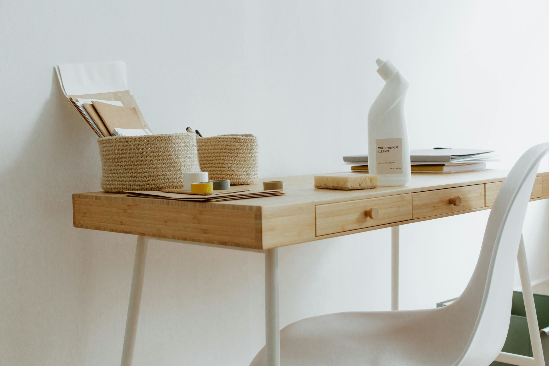 Minimal wooden desk with wicker baskets, white bottle, and white chair in a bright room