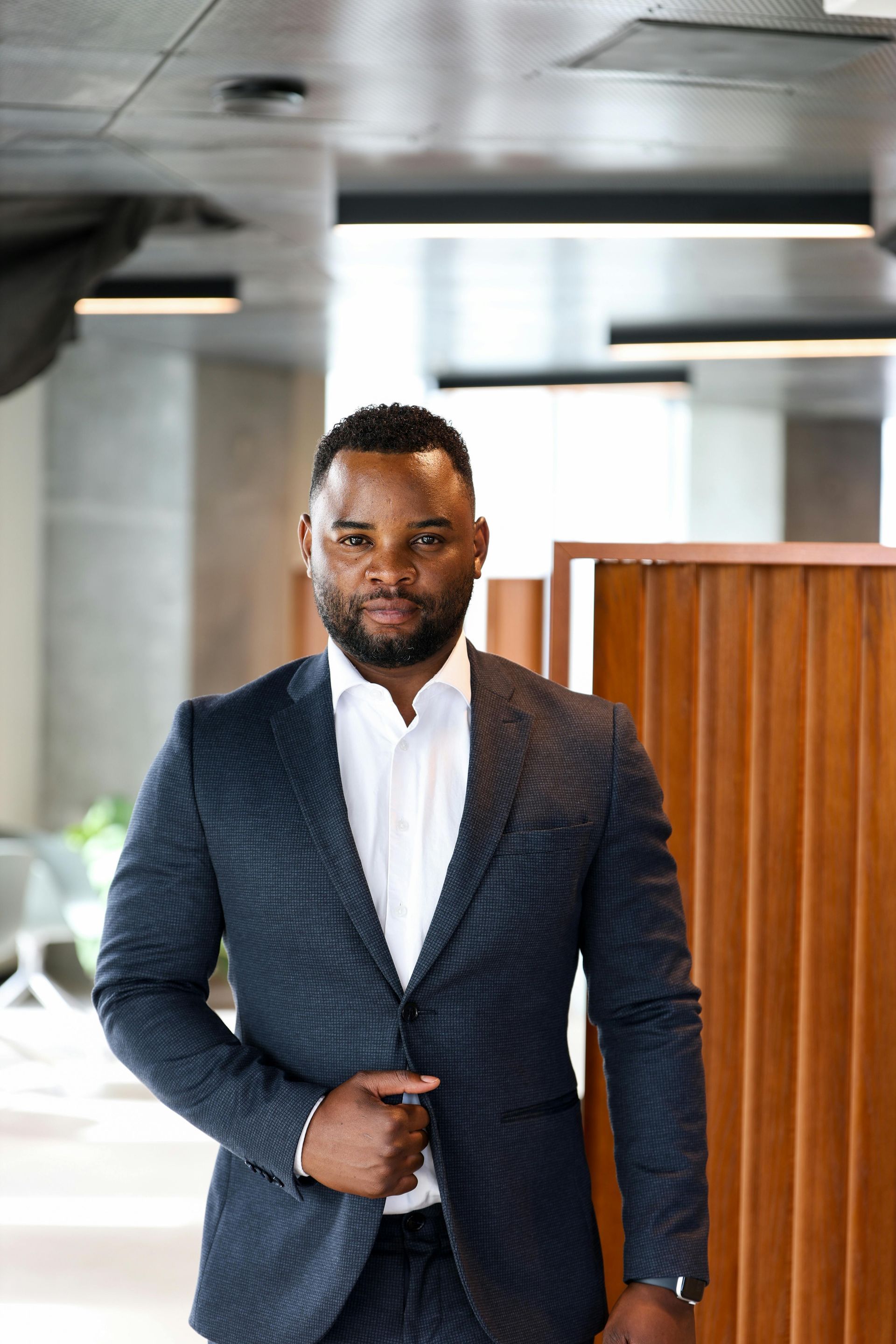 Man in a navy blazer and white shirt standing indoors in a modern office space