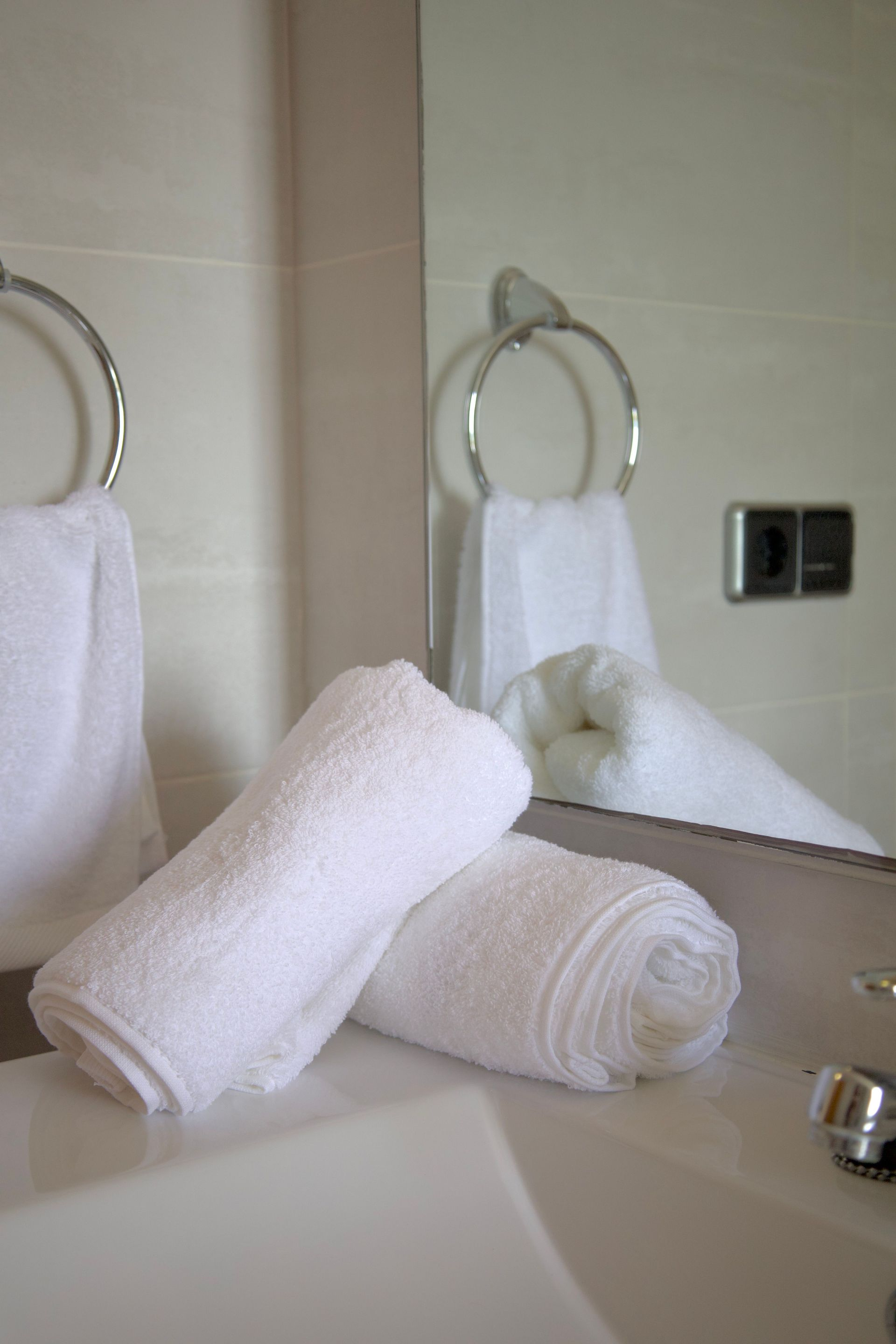 Towels rolled on a bathroom counter with a sink and wall mirror in the background