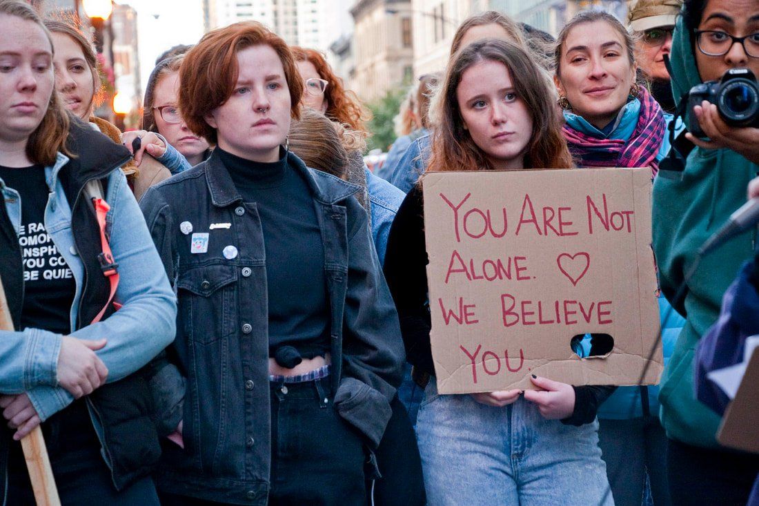 A woman is holding a sign that says `` you are not alone we believe you ''.