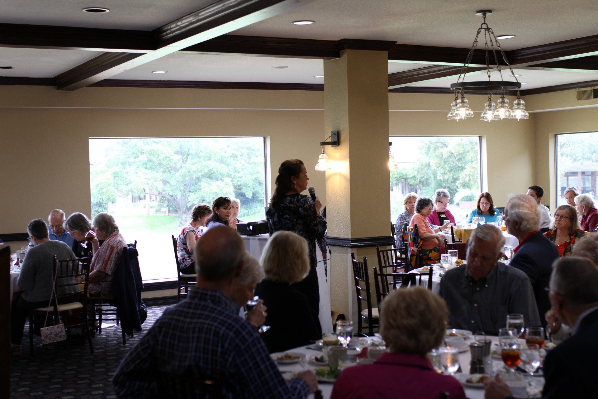A woman is giving a speech to a group of people sitting at tables in a restaurant.