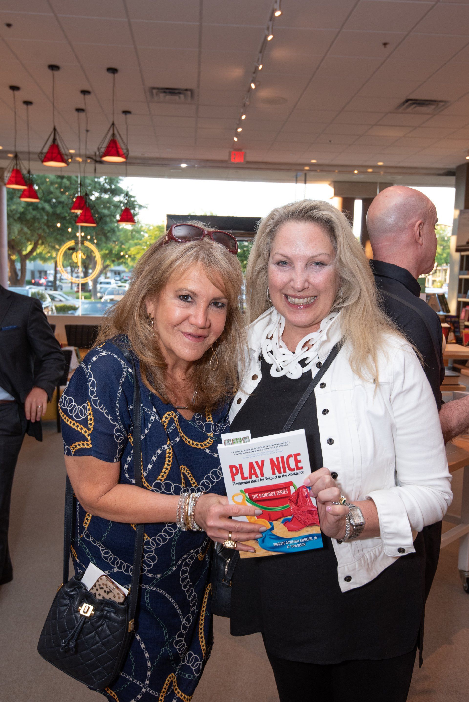 Two women are posing for a picture while holding a book titled play nice.